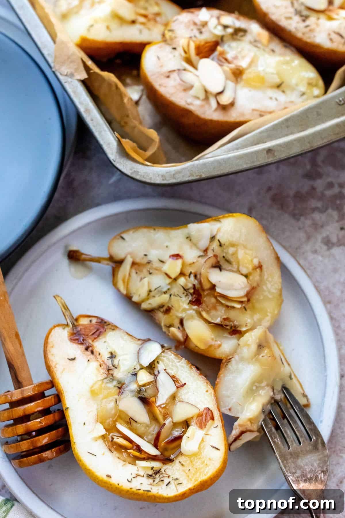 Sweet and Savory Brie Baked Pears 5 Two halves of perfectly baked pears, lavishly topped with melted brie cheese, crunchy almonds, and a sweet honey drizzle, elegantly presented on a pristine white plate with a fork, inviting a gourmet tasting experience.
