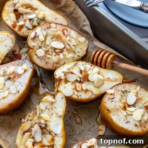 Baked pear halves on brown parchment paper with melted brie, toasted almonds, and a drizzle of honey, accompanied by plates for serving.