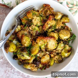 White bowl with roasted Brussels sprouts covered in Parmesan, with a silver fork.