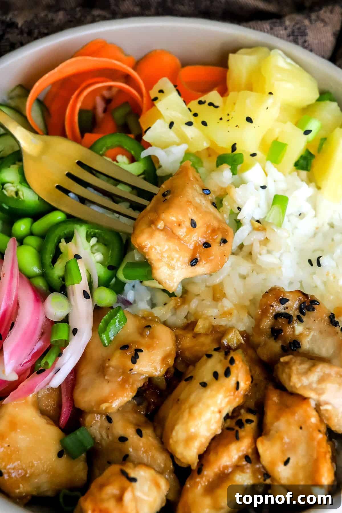 Fresh Chicken Poke Bowl 5 A close-up view of a grey ceramic bowl filled with chicken poke, showcasing the vibrant toppings and a black and gold fork on the side.