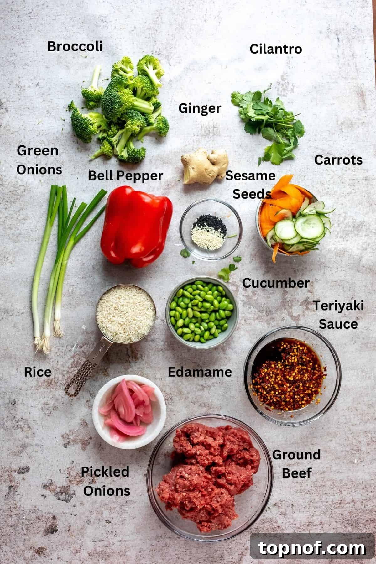 Ultimate Teriyaki Beef Bowls 3 A collection of glass bowls on a kitchen counter, each holding a different ingredient for the teriyaki beef bowls, including ground beef, chopped broccoli, diced bell peppers, and various sauce components.