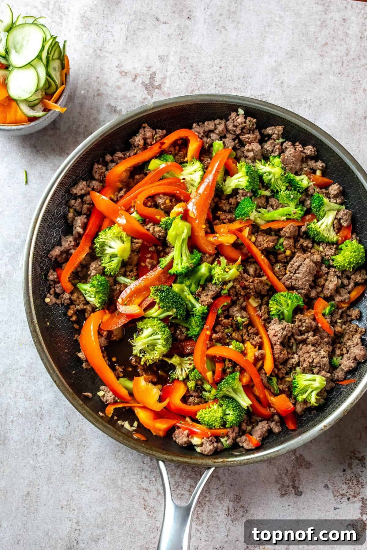 Ultimate Teriyaki Beef Bowls 4 A large non-stick skillet filled with perfectly browned ground beef, vibrant chopped broccoli, and diced bell peppers, all simmering in a rich, dark teriyaki sauce. A small bowl of extra teriyaki sauce sits beside the skillet.