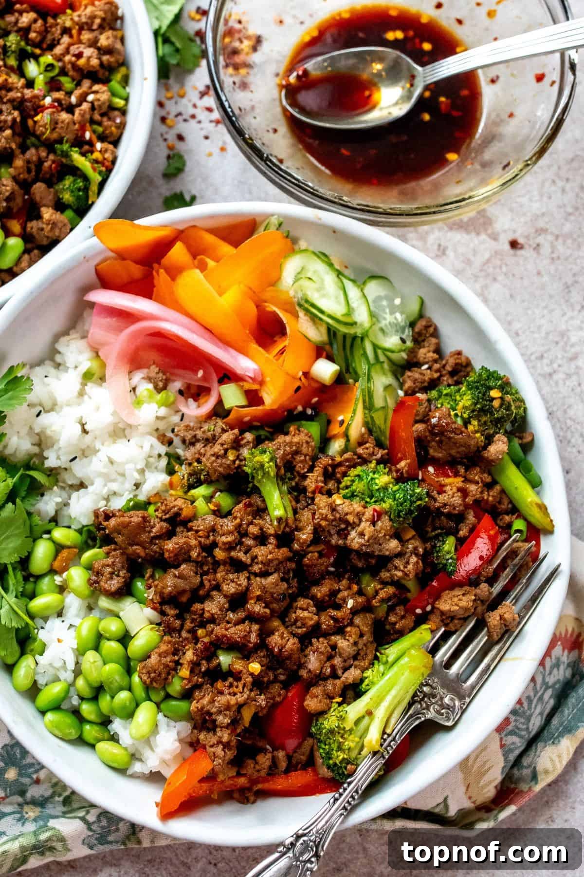 Ultimate Teriyaki Beef Bowls 5 Two white ceramic bowls identical to the first image, showcasing the fully assembled Teriyaki Beef Bowls with fresh toppings, ready to be enjoyed. A silver fork is placed beside one bowl.