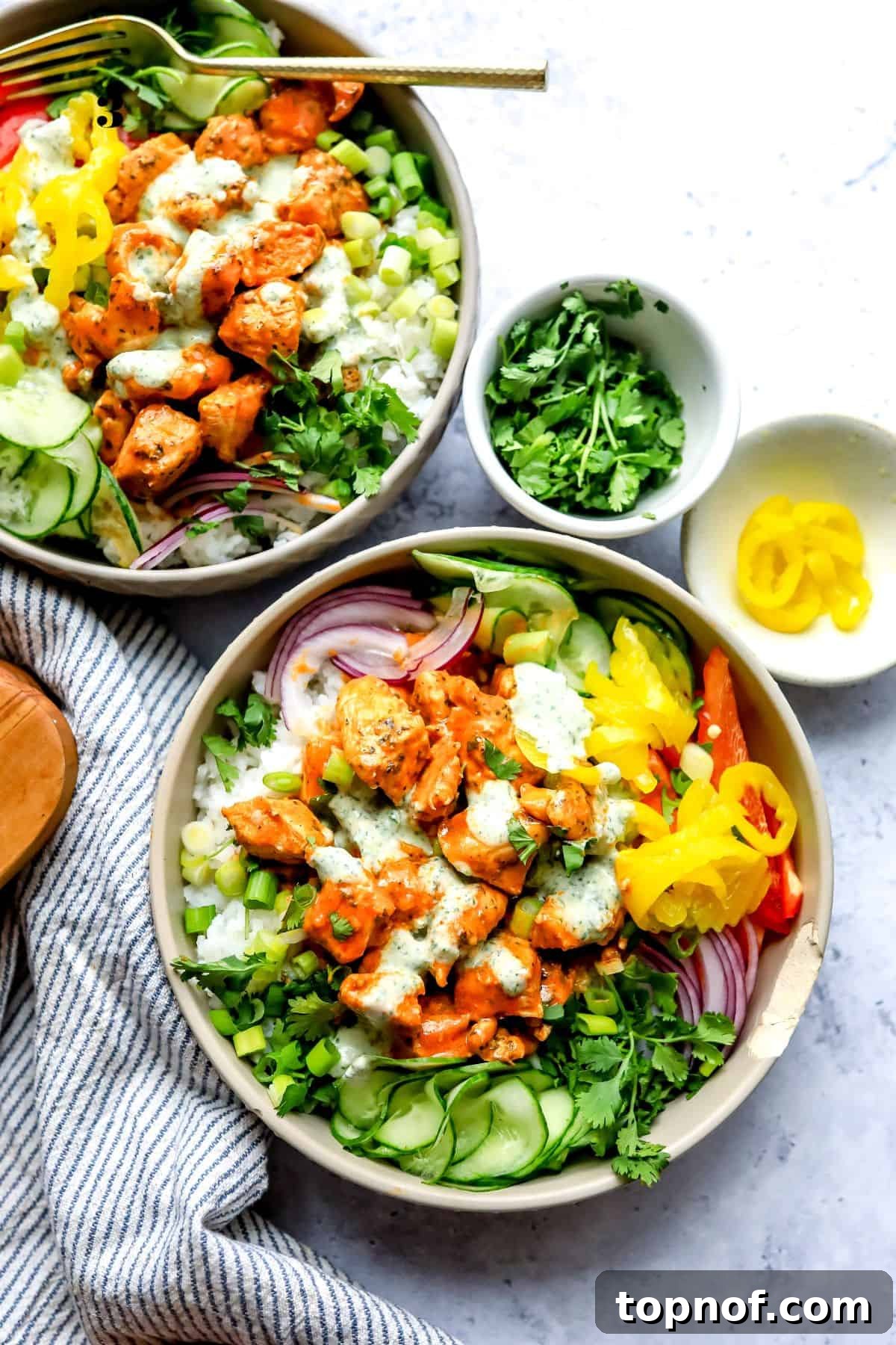 Zesty Buffalo Chicken Power Bowl 2 Two grey bowls filled with buffalo chicken, rice, and fresh vegetables. A side of cucumber slices with a generous drizzle of homemade ranch dressing.