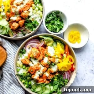 A grey bowl filled with buffalo chicken and rice, accompanied by cucumber slices and a drizzle of ranch dressing.