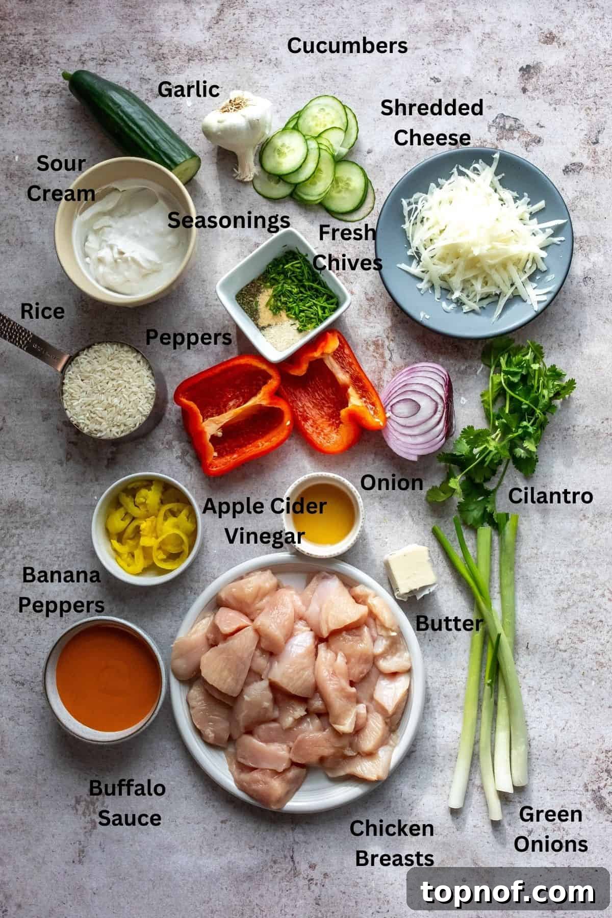 Zesty Buffalo Chicken Power Bowl 3 A curated display of ingredients for buffalo chicken bowls, including fresh cucumber, raw chicken, and various herbs and sauces arranged on plates and small bowls on a kitchen counter.