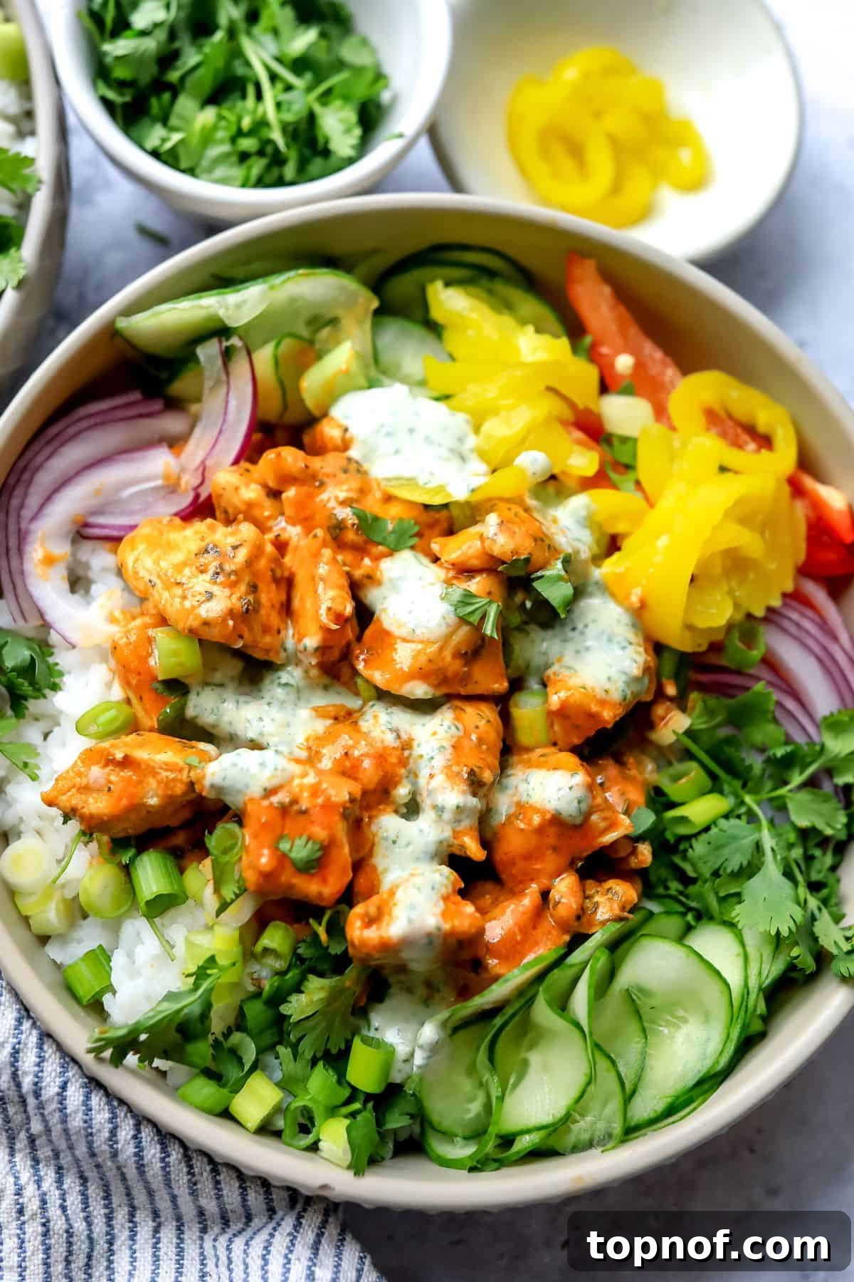 Zesty Buffalo Chicken Power Bowl 6 A close-up shot of a single grey bowl filled with buffalo chicken, rice, fresh vegetables, and a drizzle of ranch dressing, ready to be enjoyed.