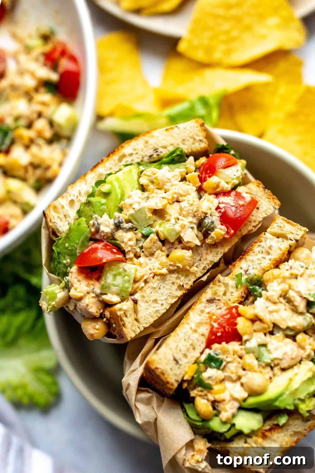 Two perfectly prepared chickpea salad sandwiches wrapped in parchment paper, presented artfully in a bowl.
