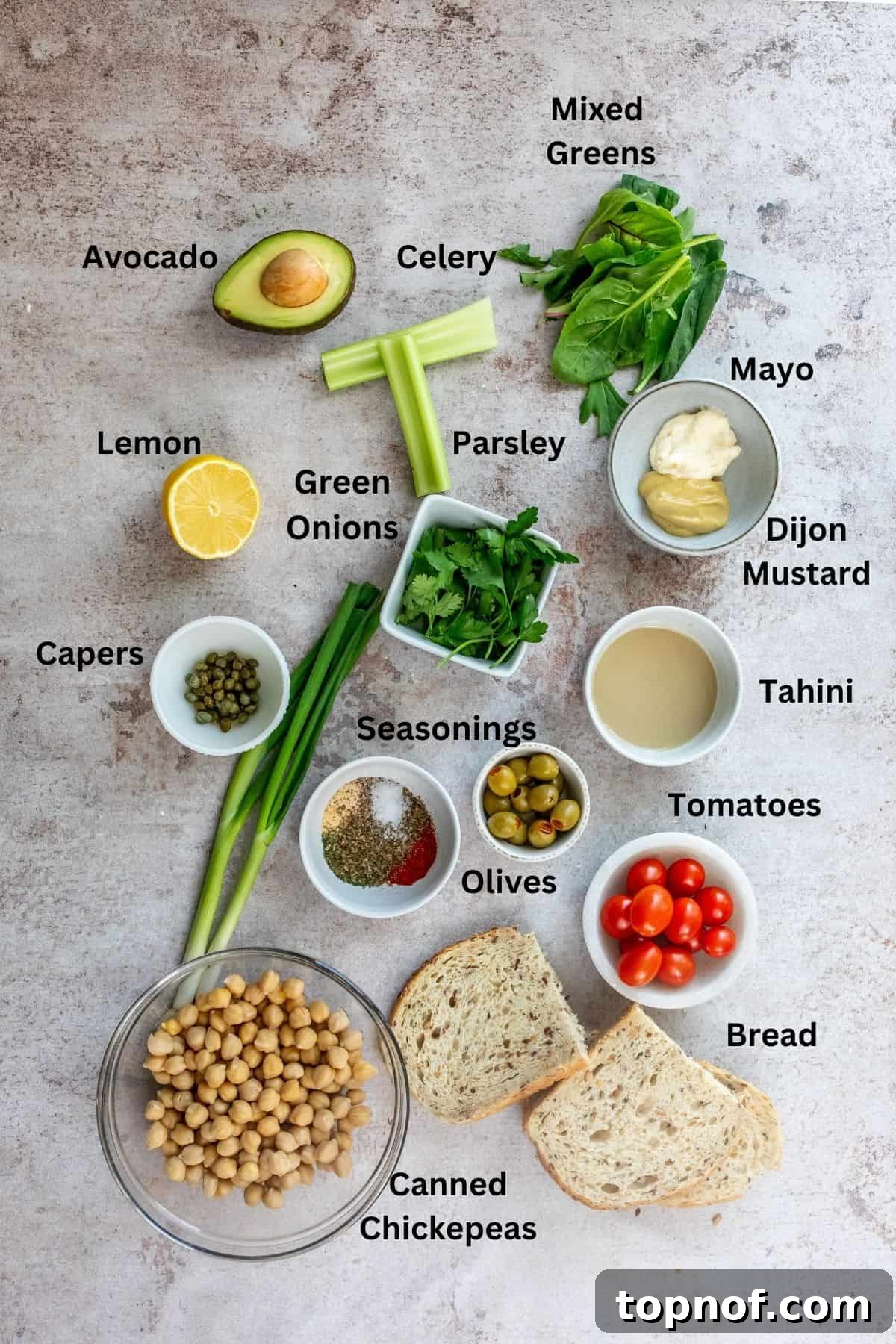 Various small bowls filled with fresh ingredients like chickpeas, chopped celery, capers, and seasonings, arranged on a kitchen counter, ready for preparation.