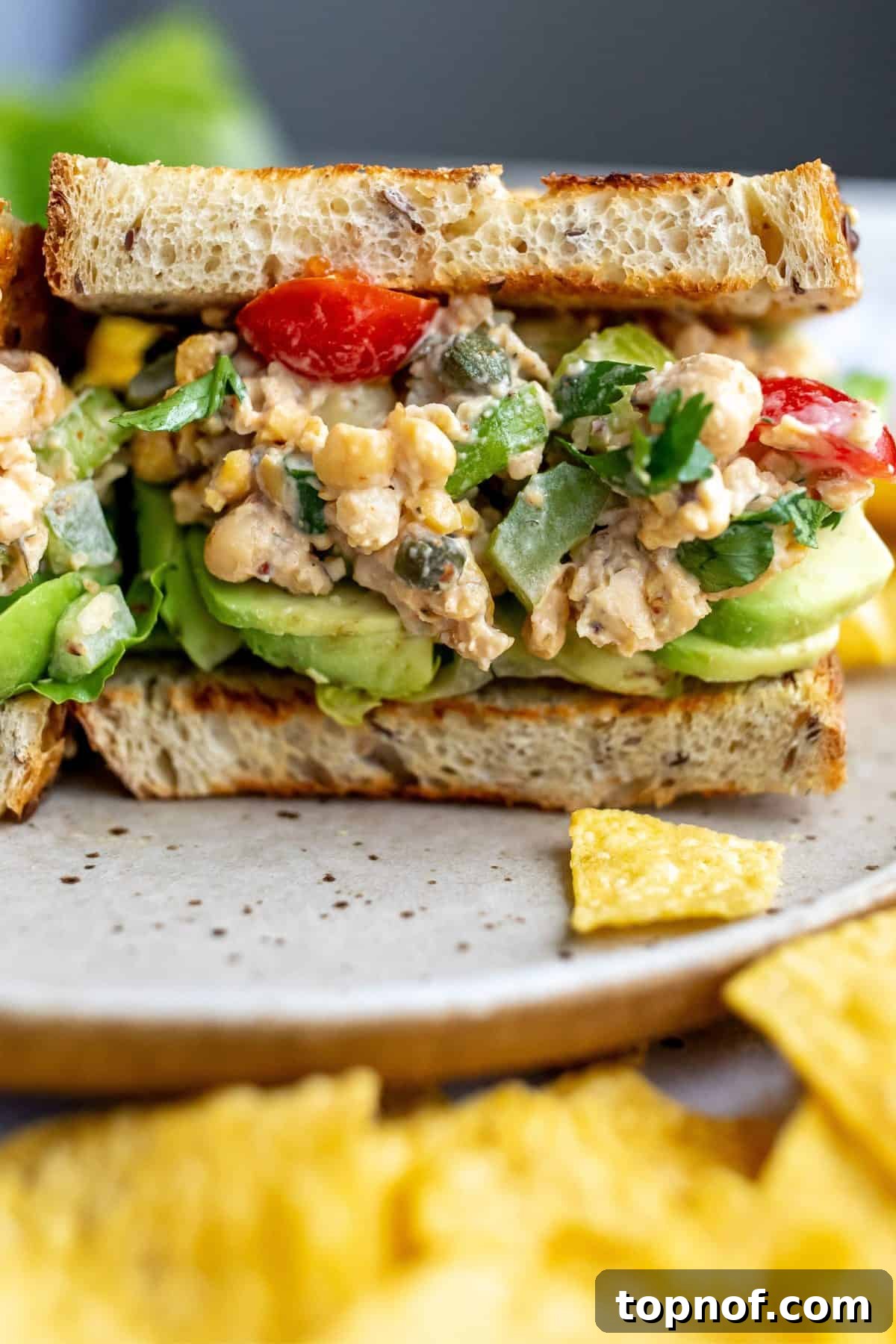 A beautifully assembled chickpea salad sandwich on a plate, accompanied by a side of crispy potato chips, ready to be enjoyed.