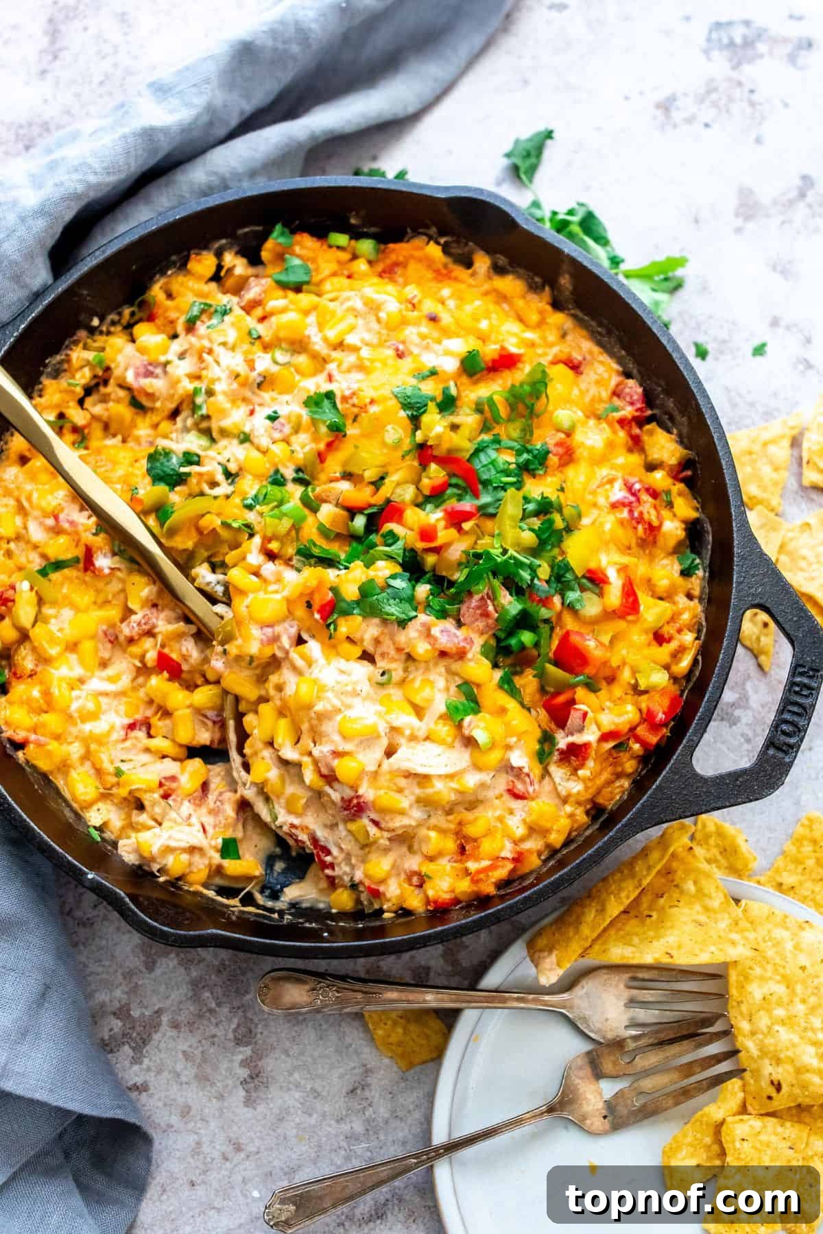 Golden Creamy Corn Delight 2 Black cast iron with corn and cream cheese mixed and topped with cilantro. Gold serving spoon in the mix to serve.