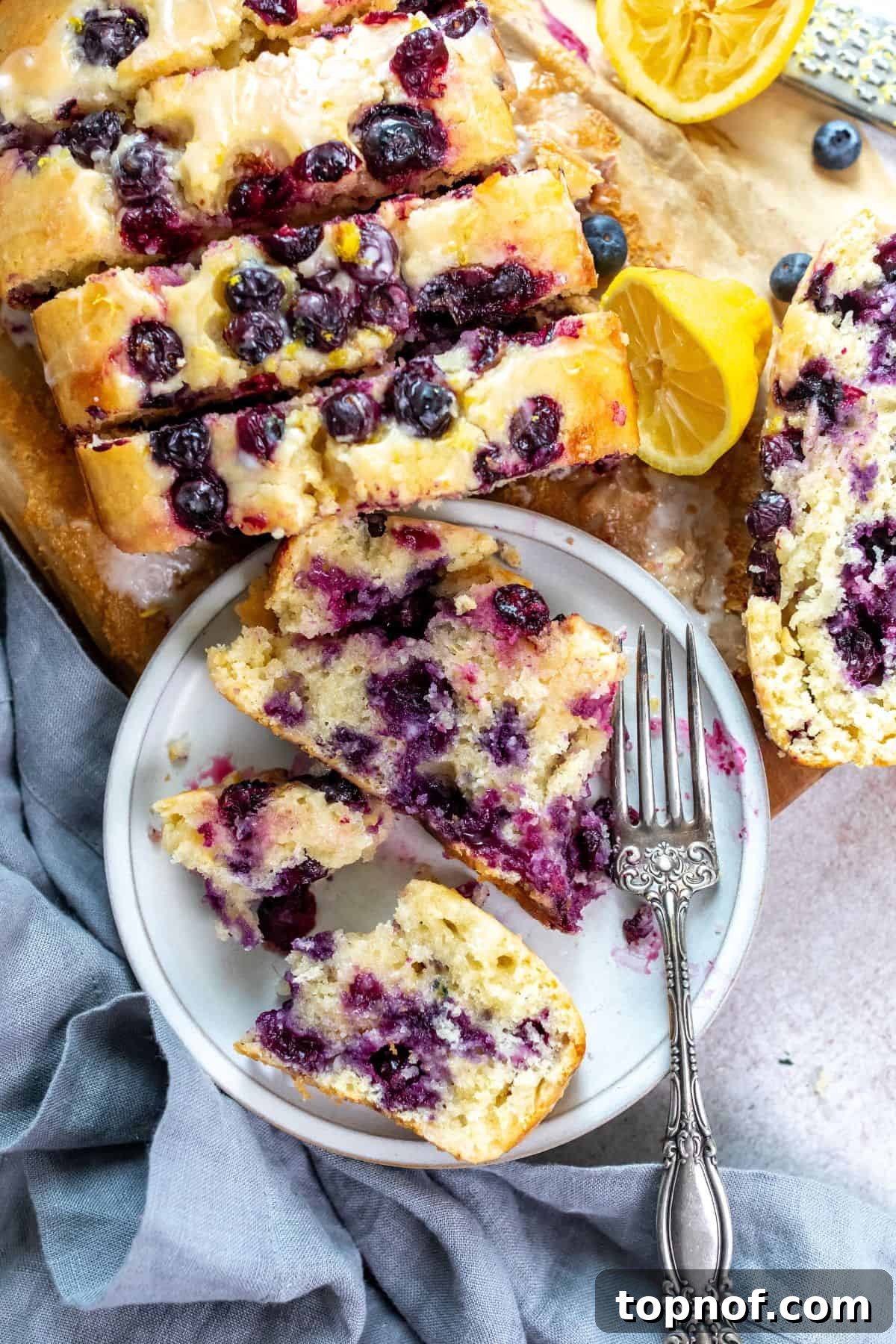 Zesty Lemon Blueberry Morning Loaf 2 A freshly baked slice of Lemon Blueberry Bread on a plate with a silver fork, garnished with fresh lemons.