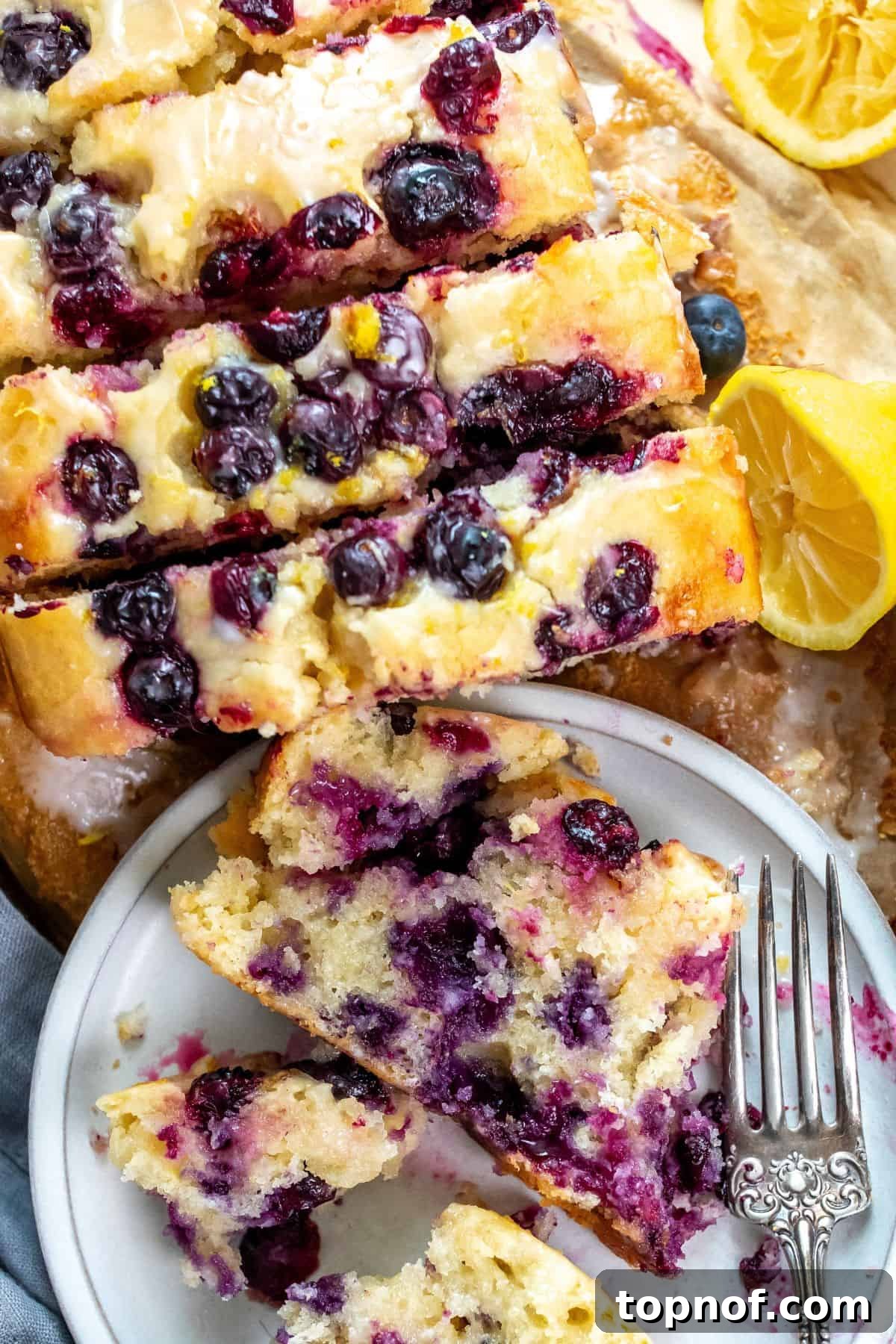 Zesty Lemon Blueberry Morning Loaf 4 A whole loaf of glazed Lemon Blueberry Bread cooling on a wire rack, with fresh lemons on the side.