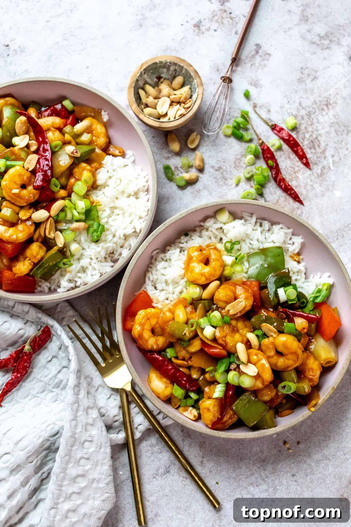Spicy Szechuan Kung Pao Shrimp 2 Pink ceramic bowls with rice and shrimp with sauce and peppers on it. Forks to the side.