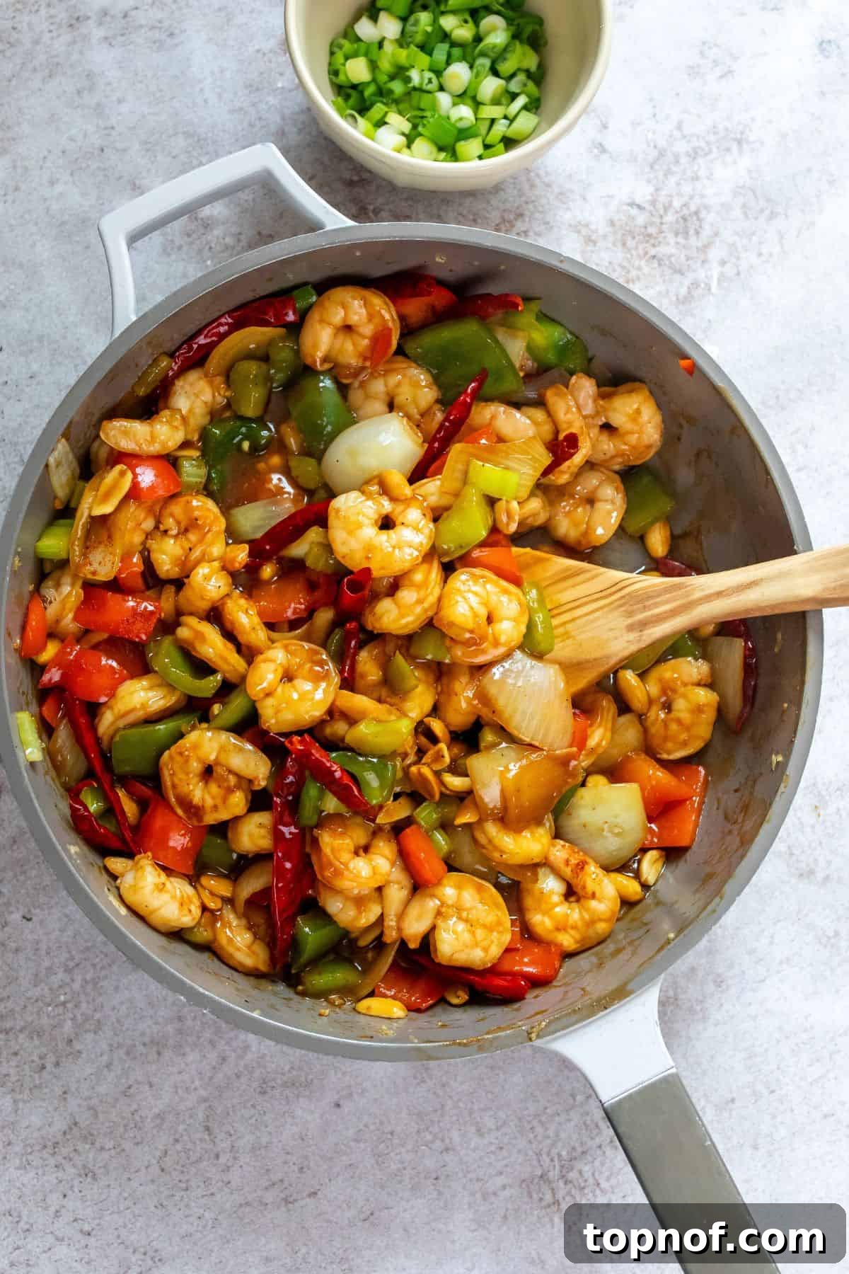 Spicy Szechuan Kung Pao Shrimp 5 Large skillet with sauce and shrimp in it, wooden spoon in the skillet.