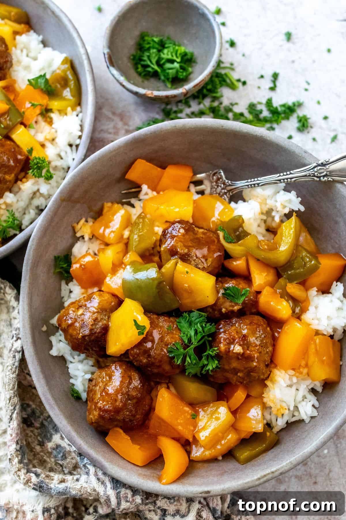Zesty Meatball Bites 6 Two grey ceramic bowls brimming with white rice, sweet and sour meatballs, and colorful bell peppers, resting on a white surface with a striped dish towel.