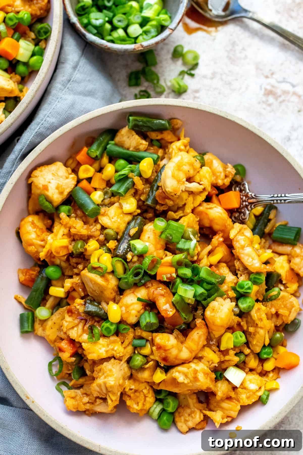 Pink bowls with chicken and shrimp in them, fresh veggies mixed in. Grey kitchen towel and a spoon on the side.