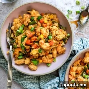 Pink bowls with chicken and shrimp in them, fresh veggies mixed in. Grey kitchen towel and a spoon on the side.
