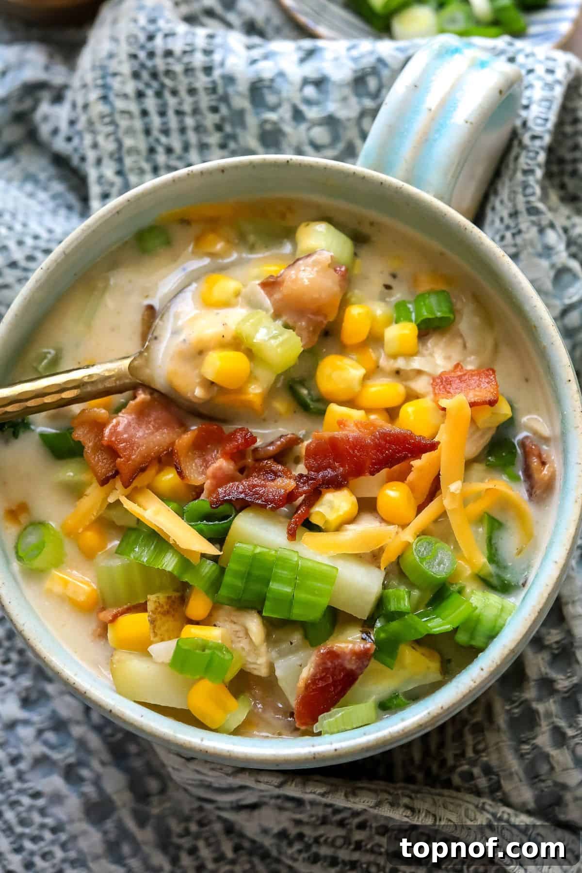 Golden Chicken Corn Chowder 6 Soup mug with a handle on a counter with corn chowder and bacon on top. Gold spoon to the side.
