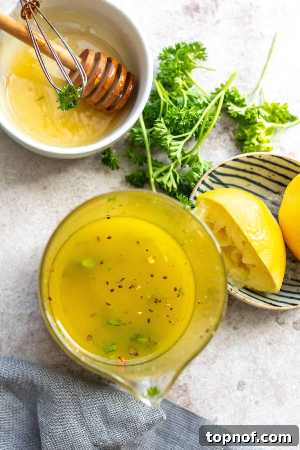 Bright Lemon Honey Dressing 2 Glass jar with freshly made lemon honey dressing. Fresh lemons and a bottle of olive oil are neatly arranged beside it.