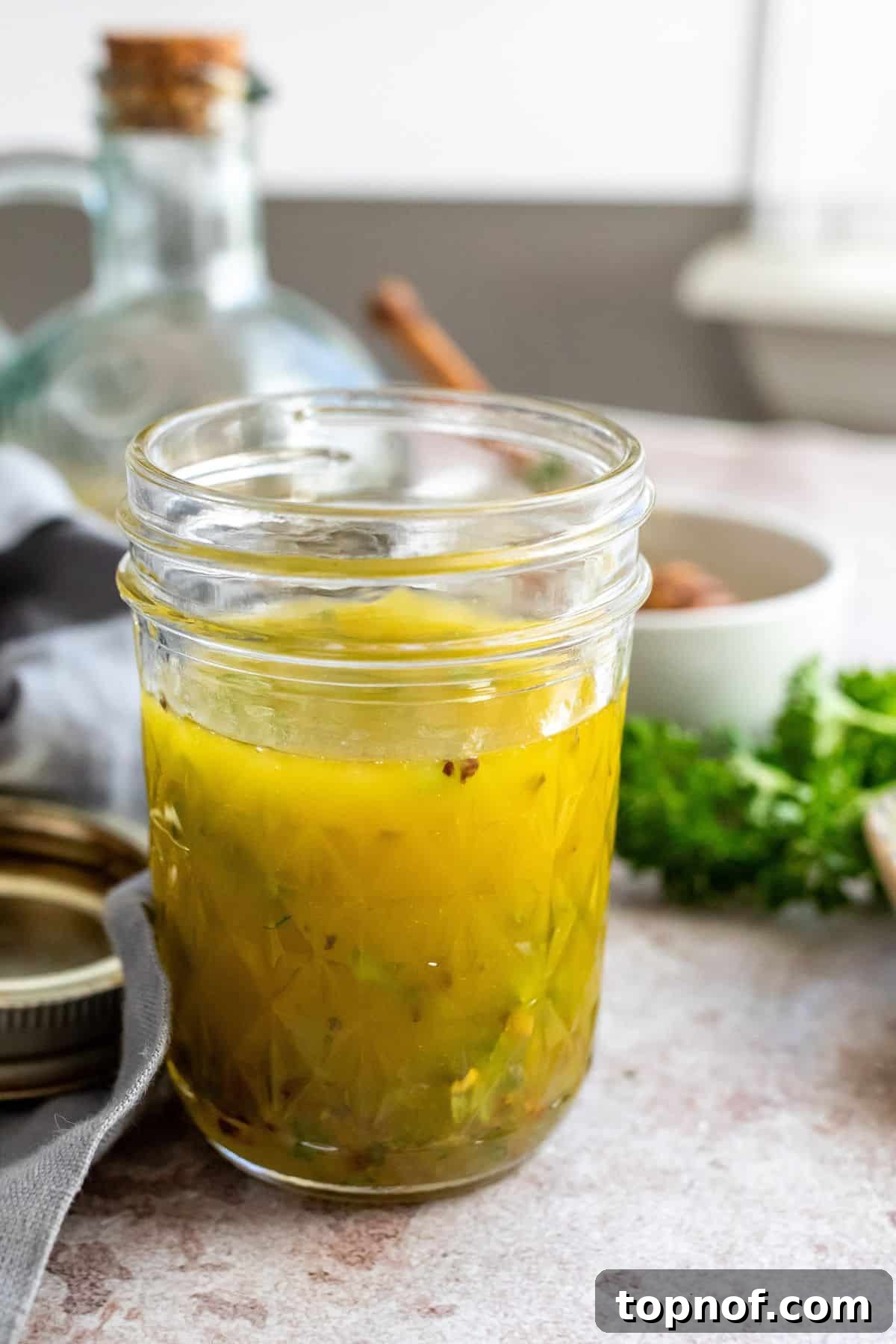 Bright Lemon Honey Dressing 4 A glass jar filled with golden lemon honey dressing, ready to be shaken. A bottle of olive oil and fresh lemons are in the background.