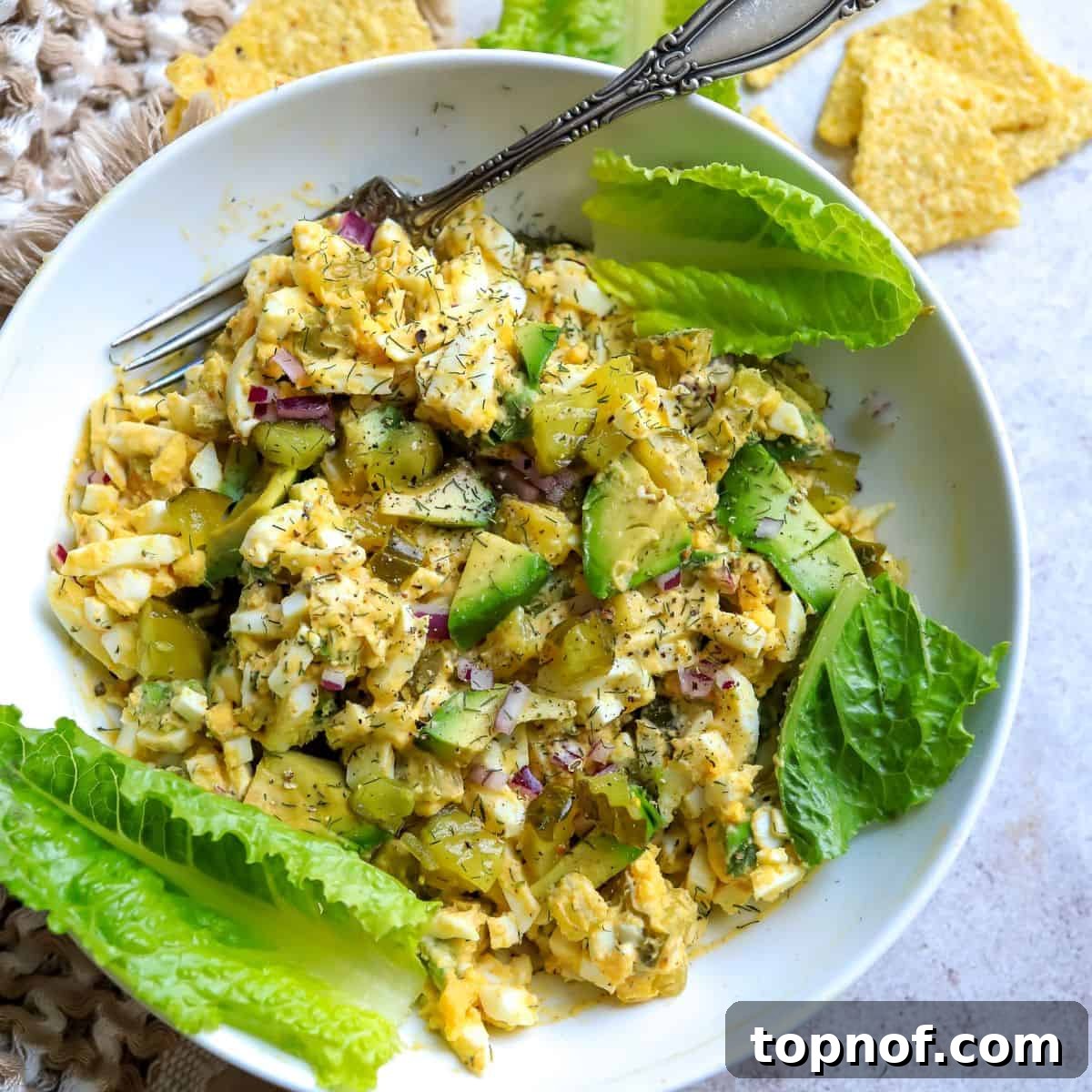 A white bowl containing a creamy mix of egg and avocado, garnished with lettuce, presenting a healthier take on a classic salad.