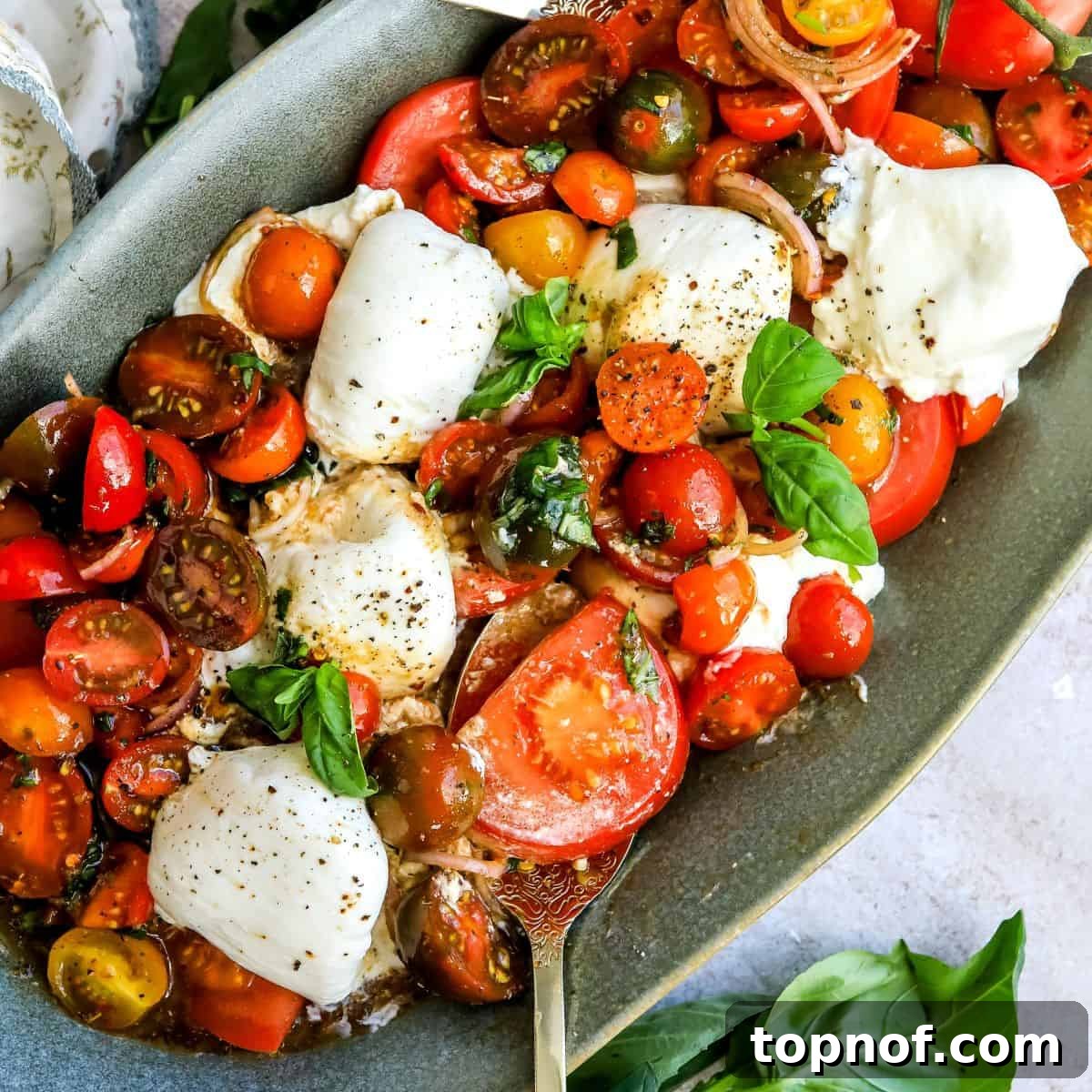 A vibrant green serving dish showcasing a Tomato Burrata Salad, generously topped with fresh basil, dressing, and seasoning.