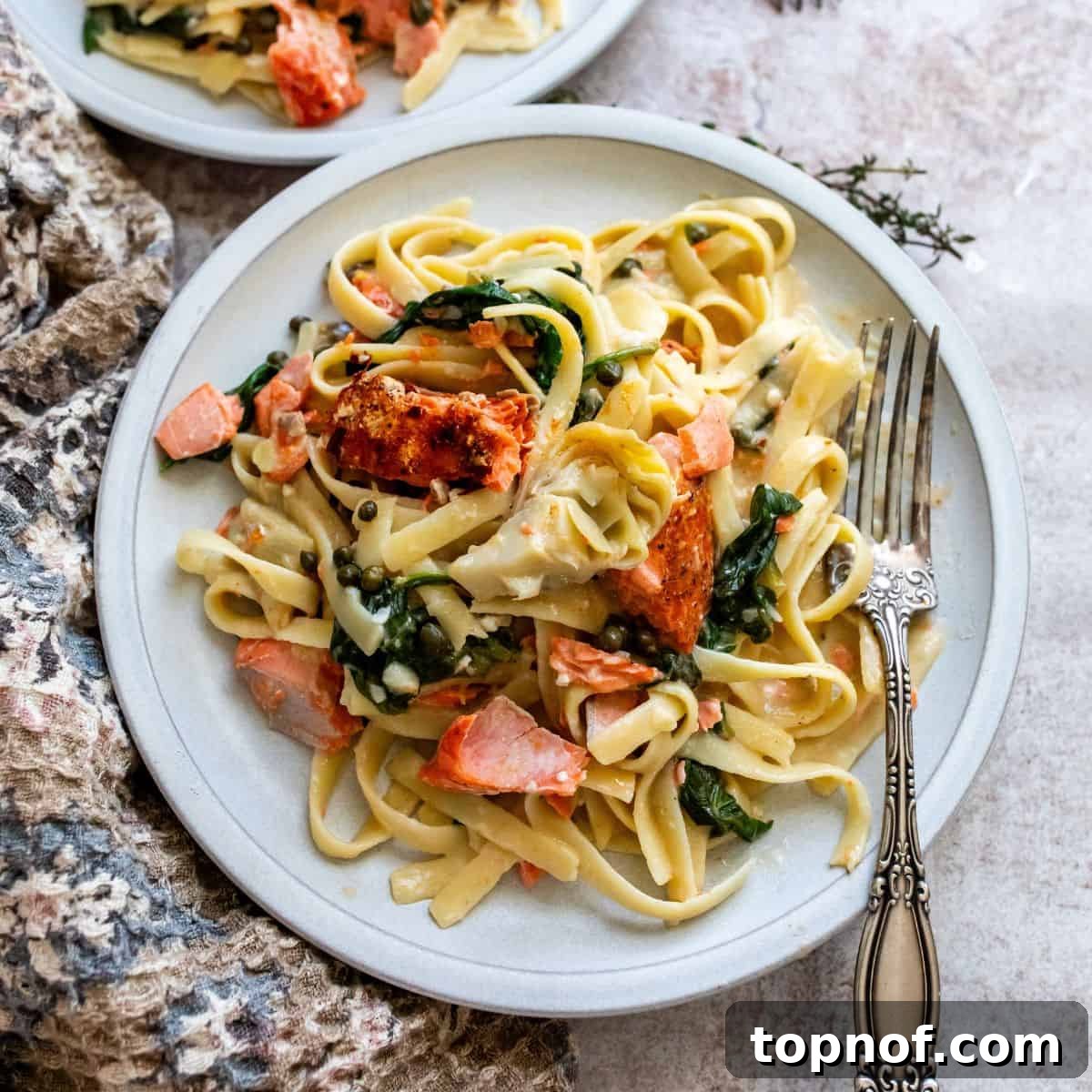 White ceramic plate featuring creamy pasta topped with perfectly baked salmon and a silver fork on the side.