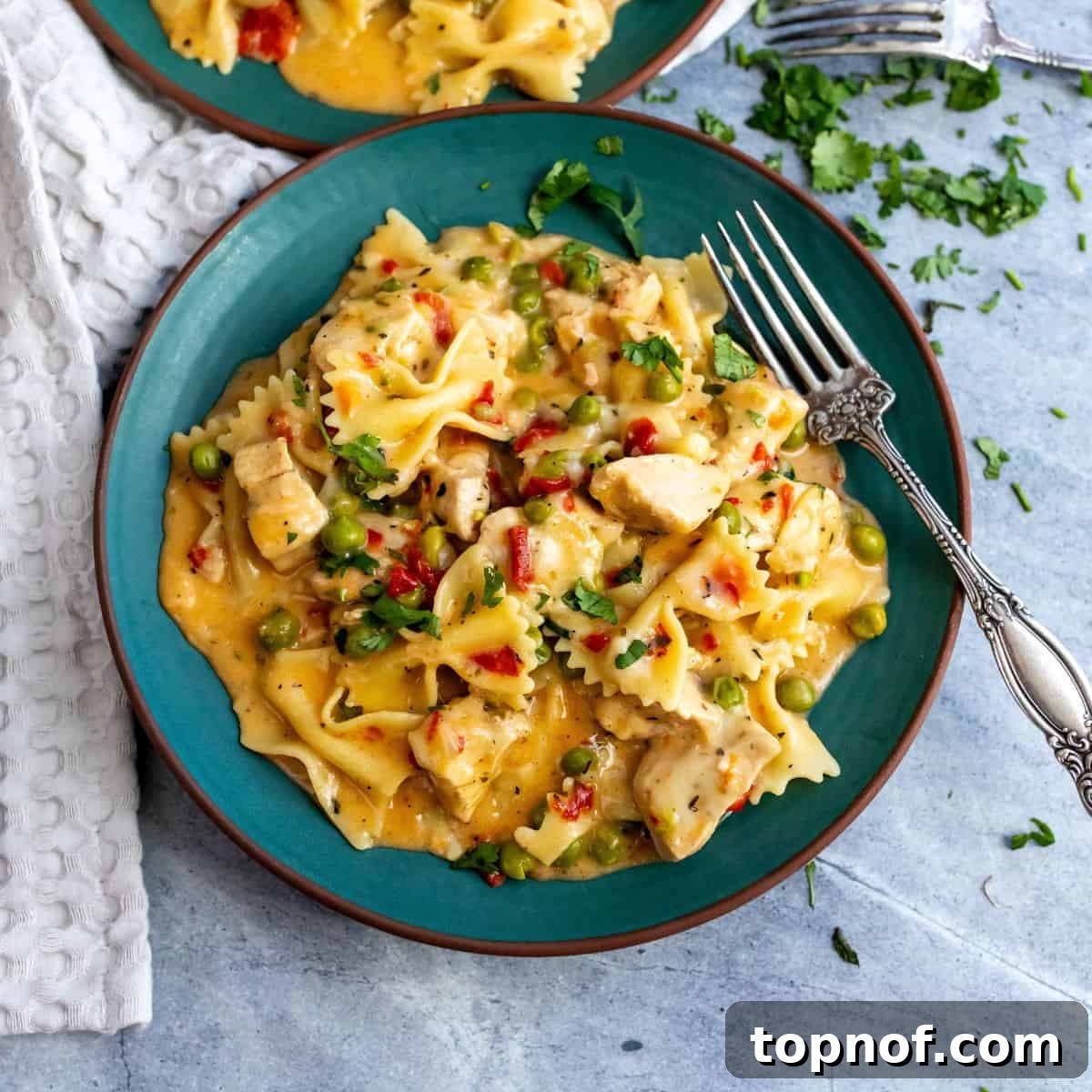 Green ceramic plate with creamy cheesy chicken pasta, garnished with fresh cilantro and a silver fork on the side.