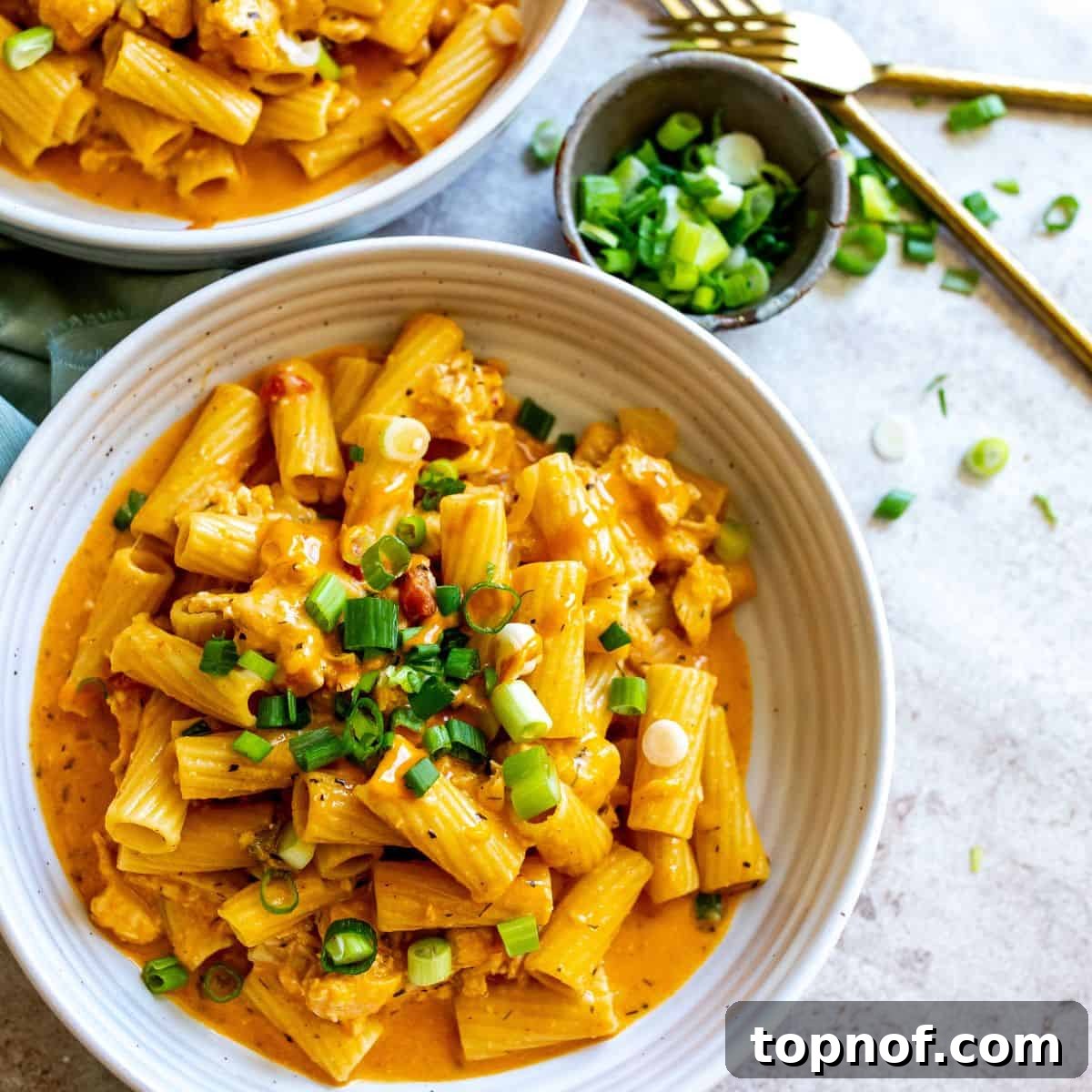 Two white ceramic bowls brimming with saucy buffalo chicken pasta, served with gold forks on the side.