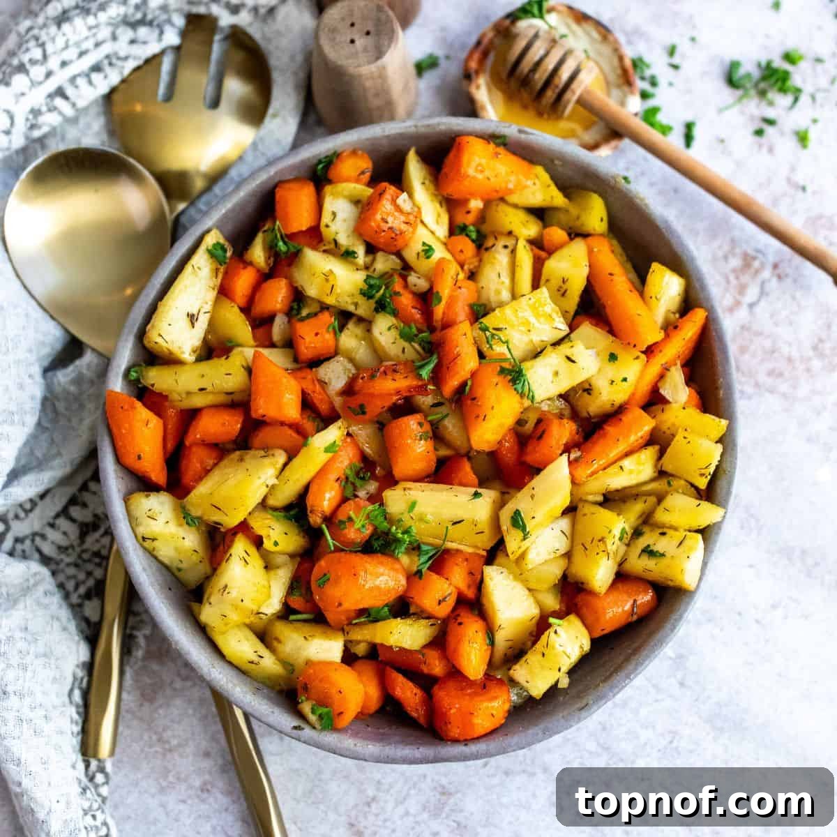 Grey pottery bowl with perfectly roasted carrots and parsnips, with honey on the side.