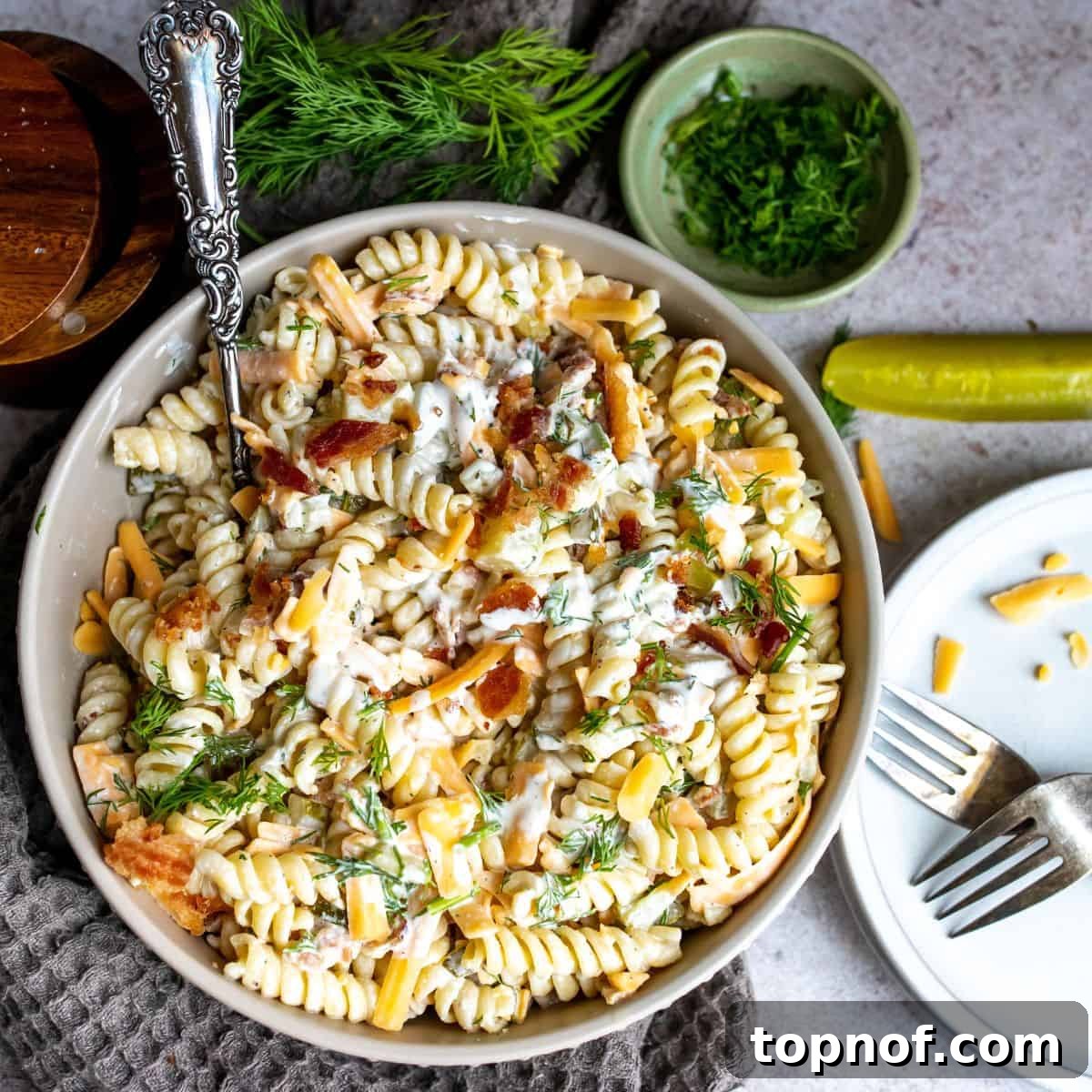 Grey bowl with pasta and bacon, garnished with pickles, forming a delicious Dill Pickle Salad.