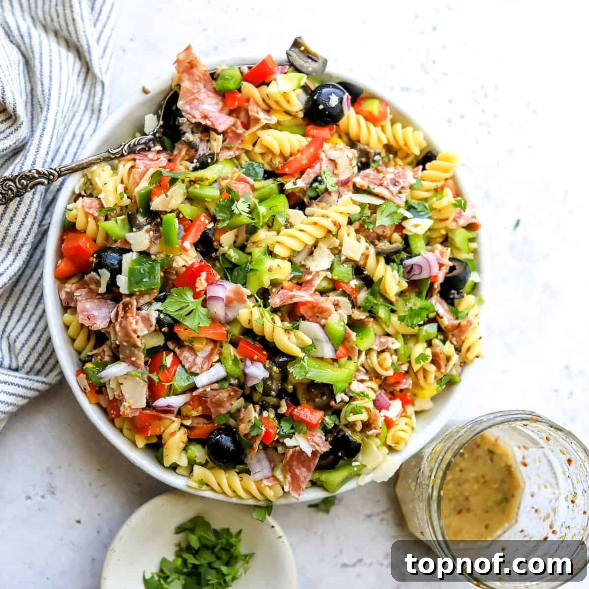 White ceramic bowl with zesty pasta salad and Italian dressing on the side.