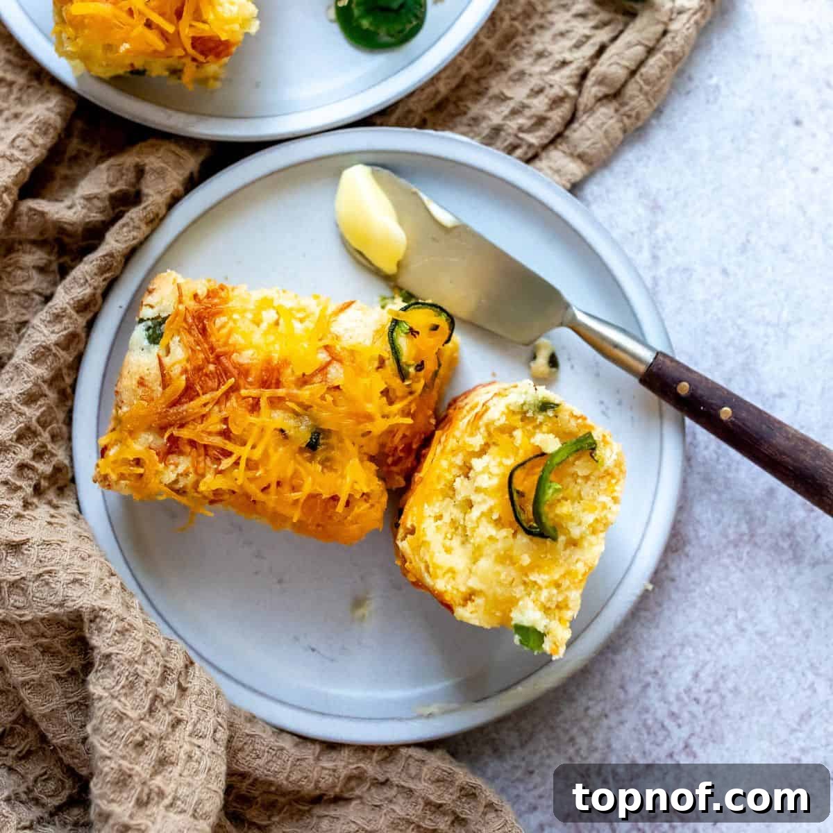 Small white plate with cornbread and jalapeños, accompanied by a butter knife with butter.