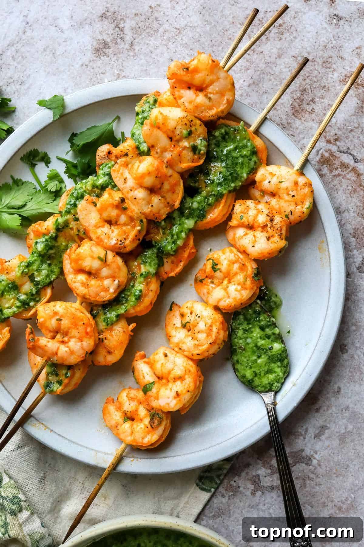 Oven-Kissed Shrimp Skewers 2 Perfectly cooked oven-baked shrimp skewers served on a white plate with a side of vibrant green pesto and a fork, ready to be enjoyed.