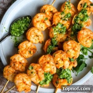 Delicious oven-baked shrimp skewers on a white plate with a side of sauce, ready to serve.
