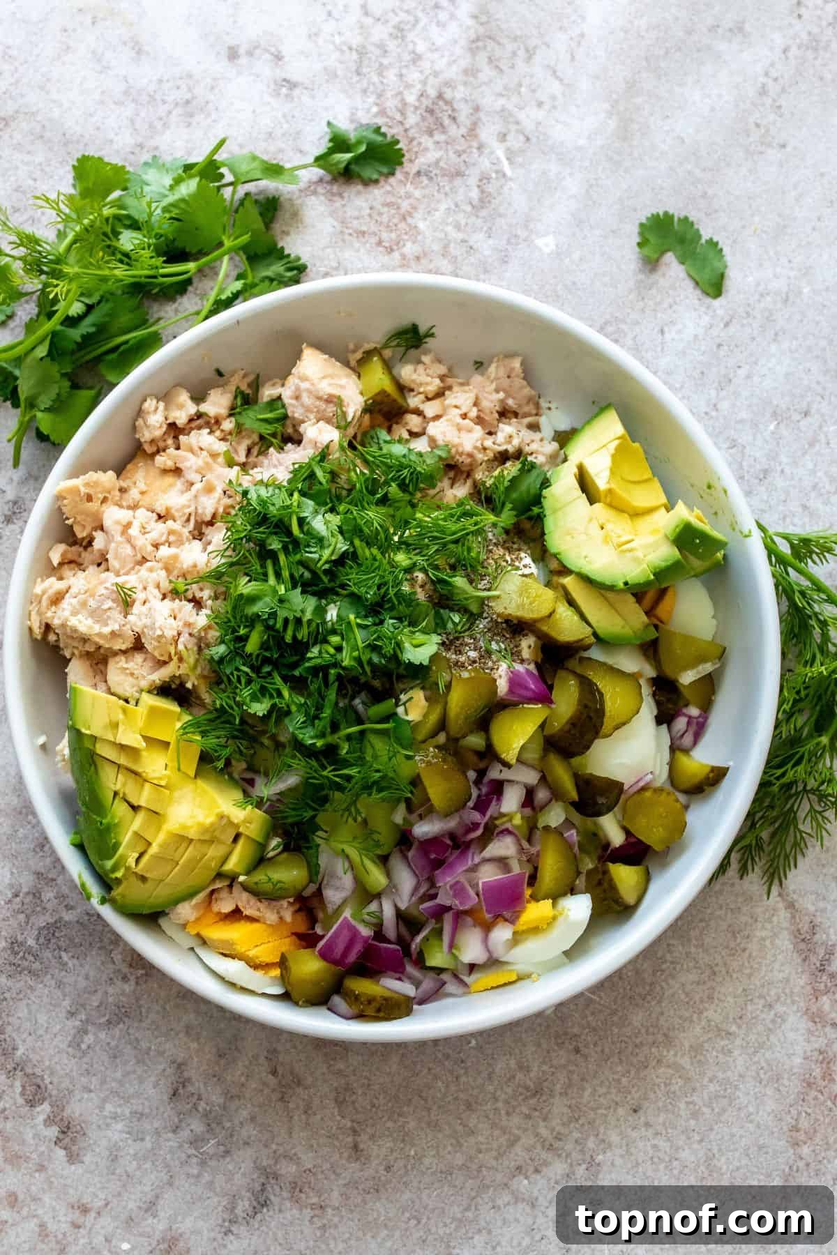 Creamy Tuna & Egg Fusion 4 A white bowl filled with all the combined ingredients for tuna and egg salad, showing the vibrant mix of tuna, eggs, and fresh vegetables, ready for final mixing.