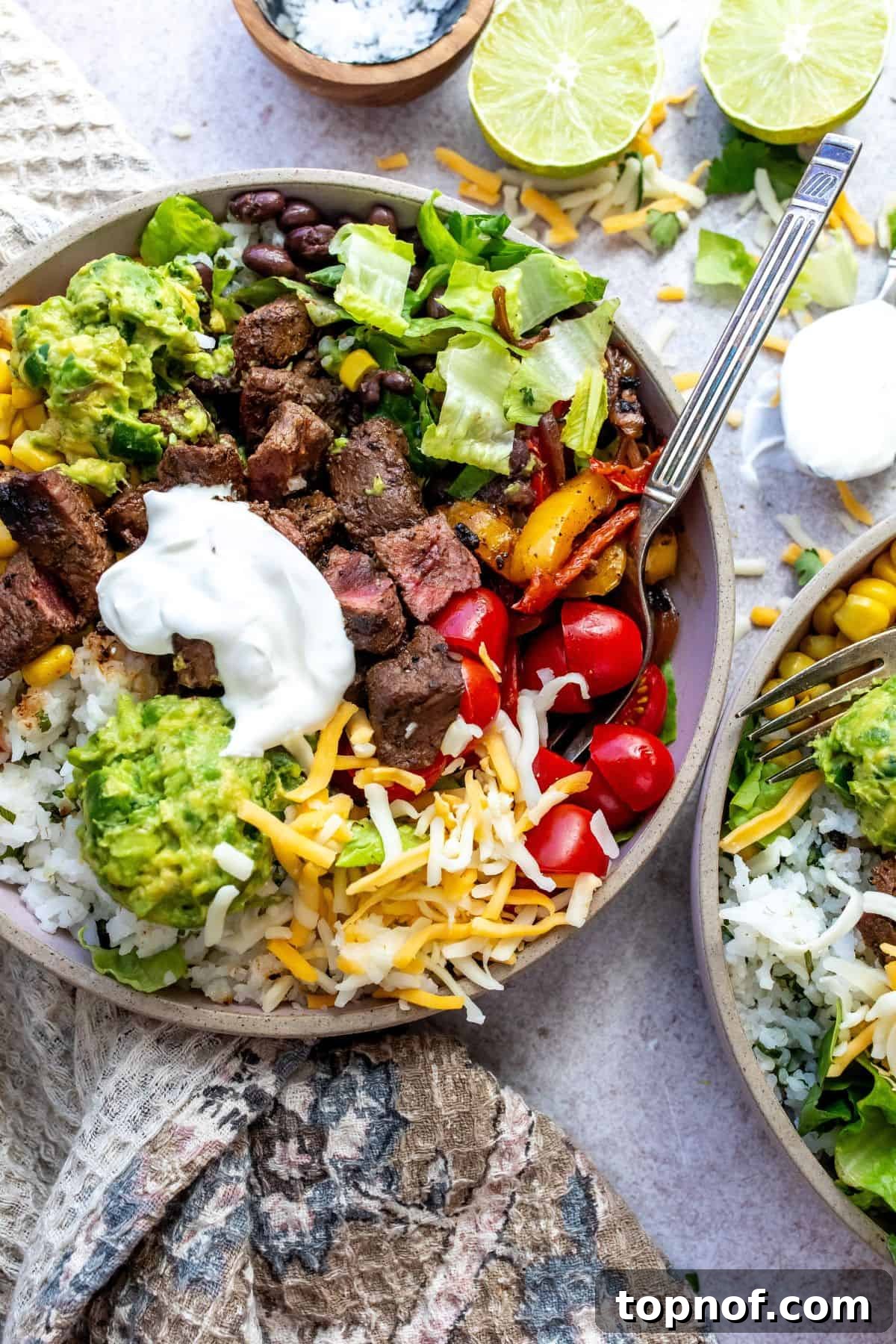 Hearty Steak and Rice Bowls 2 A ceramic bowl brimming with tender chipotle steak and rice, generously loaded with fresh toppings like corn, black beans, salsa, and guacamole, ready to be enjoyed with a fork.