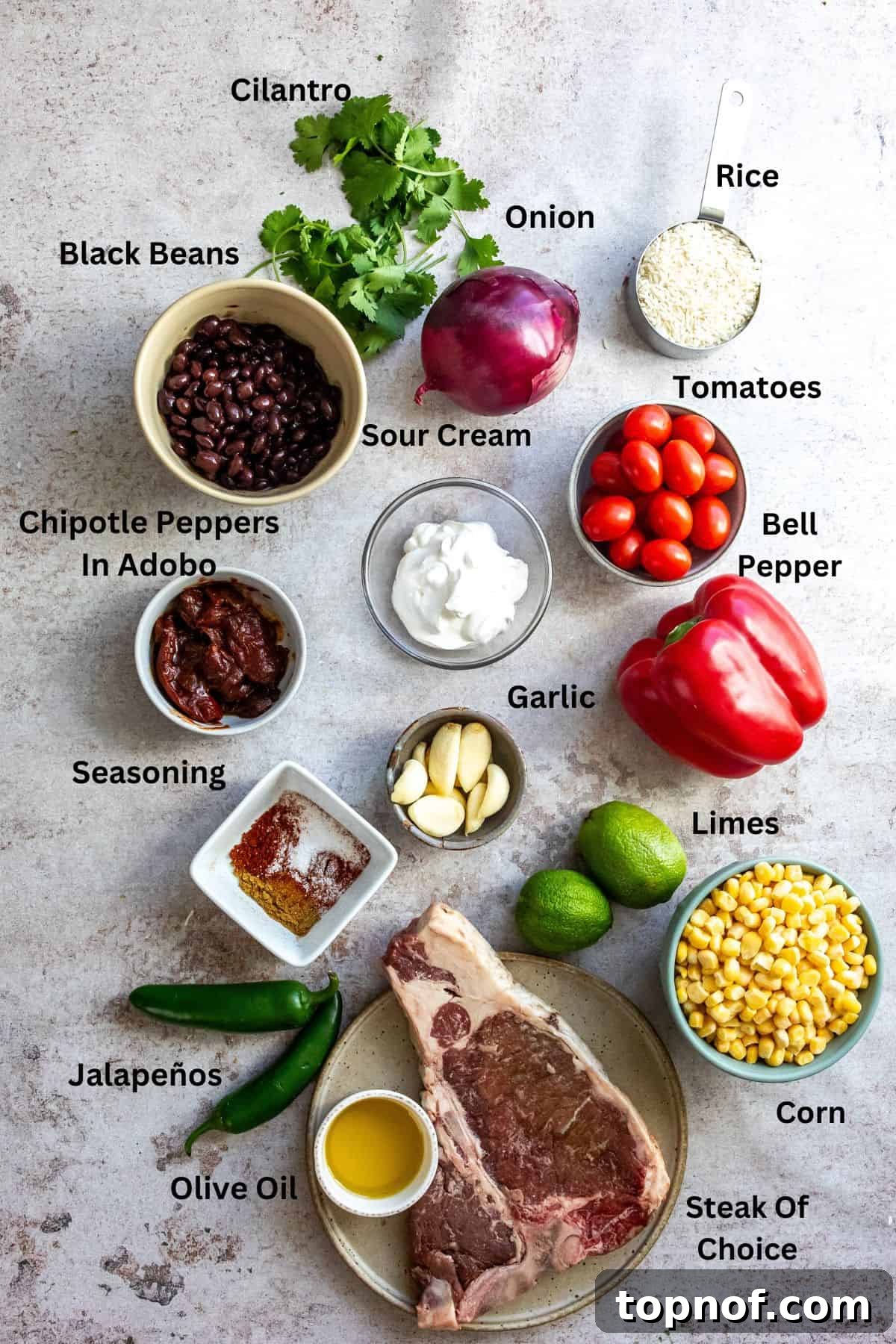 Hearty Steak and Rice Bowls 3 An organized display of fresh ingredients for Chipotle Steak Bowls on a kitchen counter, including raw steak, colorful bell peppers, red onion, corn, black beans, lime, cilantro, and chipotle peppers in adobo.