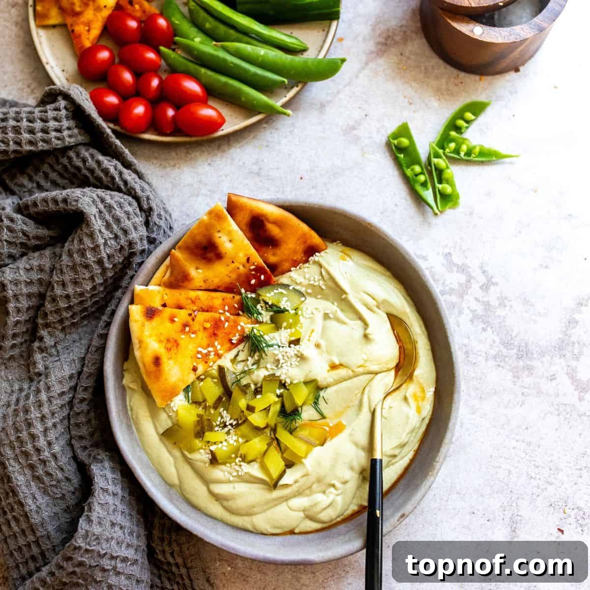 Creamy Dill Pickle Hummus in a gray bowl with a spoon, surrounded by fresh vegetable dippers.
