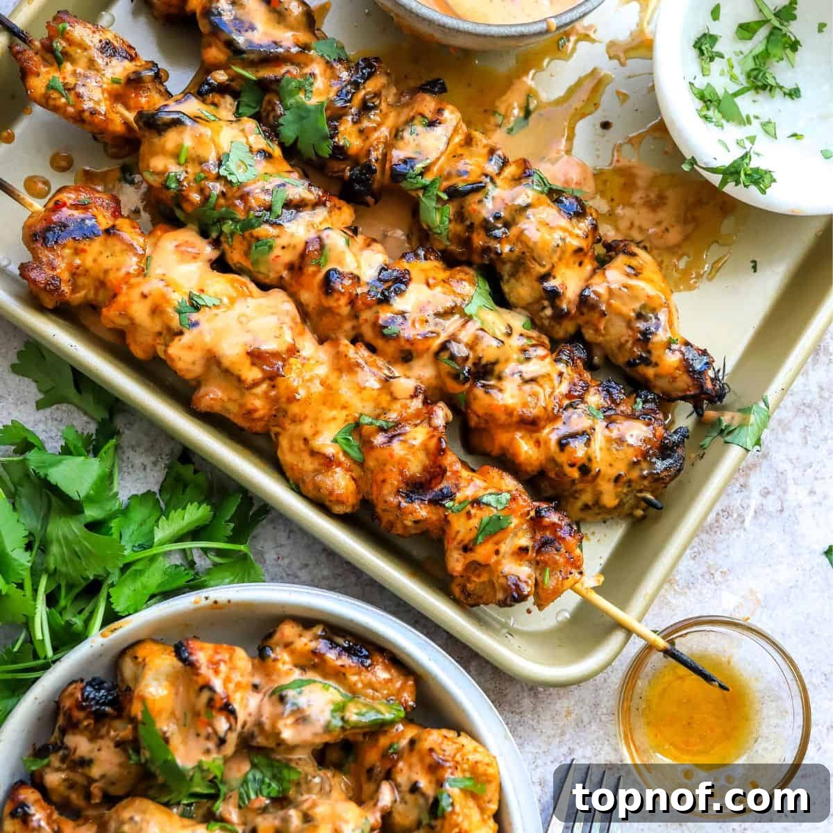 Baking sheet with spicy Bang Bang Chicken Skewers, with a bowl of air-fried skewers on the side.