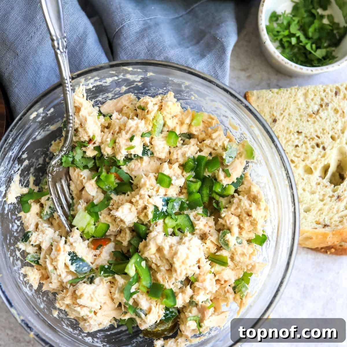Tuna salad in a clear bowl, garnished with jalapeño, and served with gluten-free bread slices.