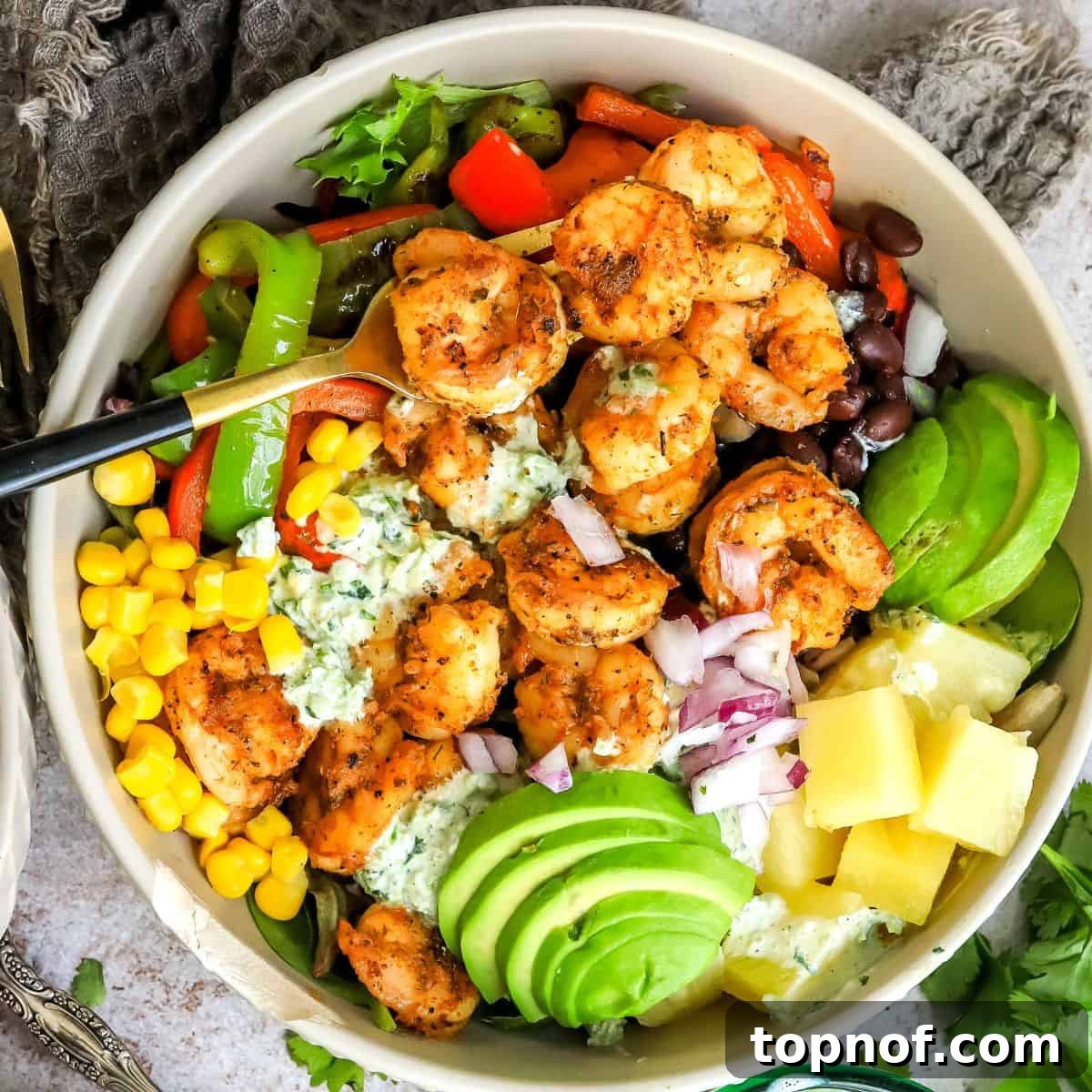 Grey bowls showcasing vibrant salad topped with blackened shrimp, accompanied by a stylish gold fork.