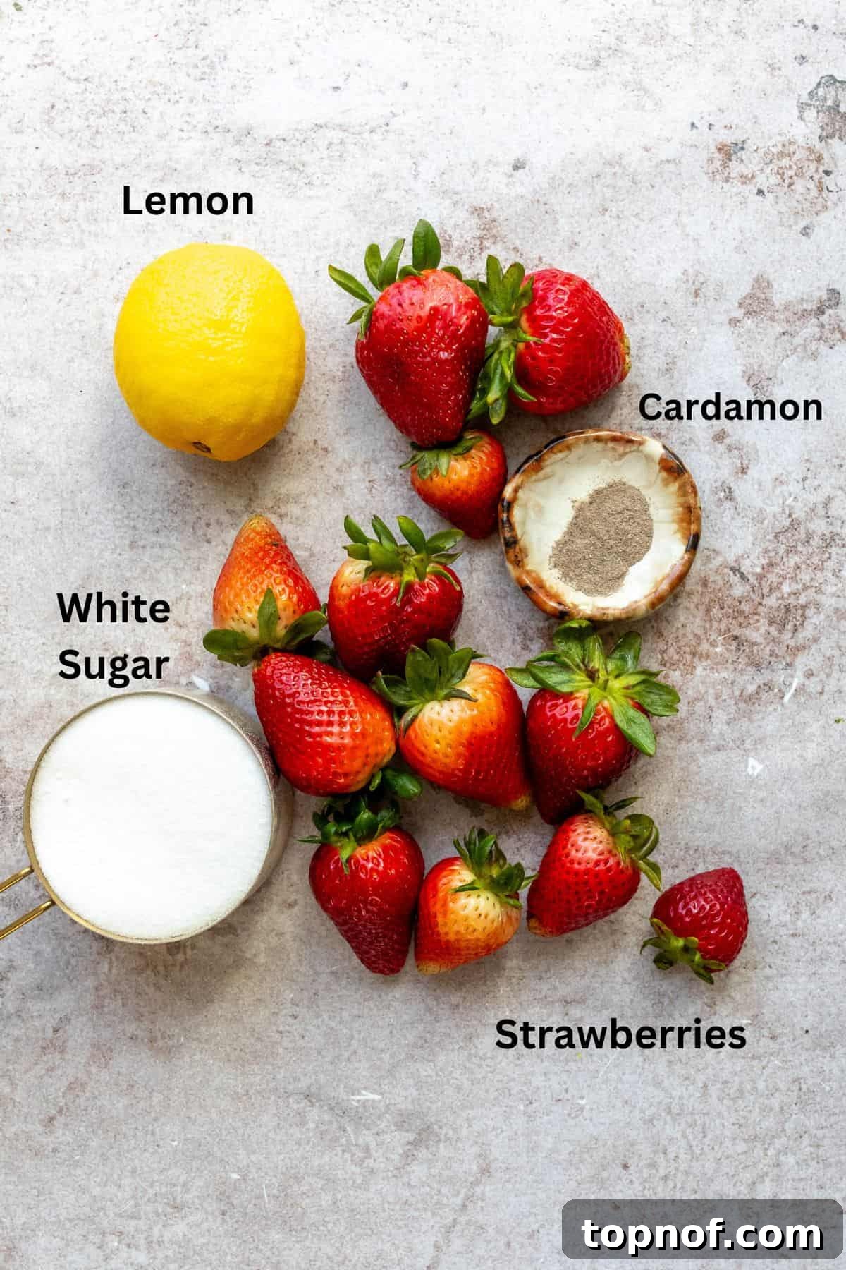 An overhead image of the key ingredients for homemade strawberry jam laid out on a flat surface: vibrant fresh strawberries, sparkling white granulated sugar, and a small bowl of freshly squeezed lemon juice.