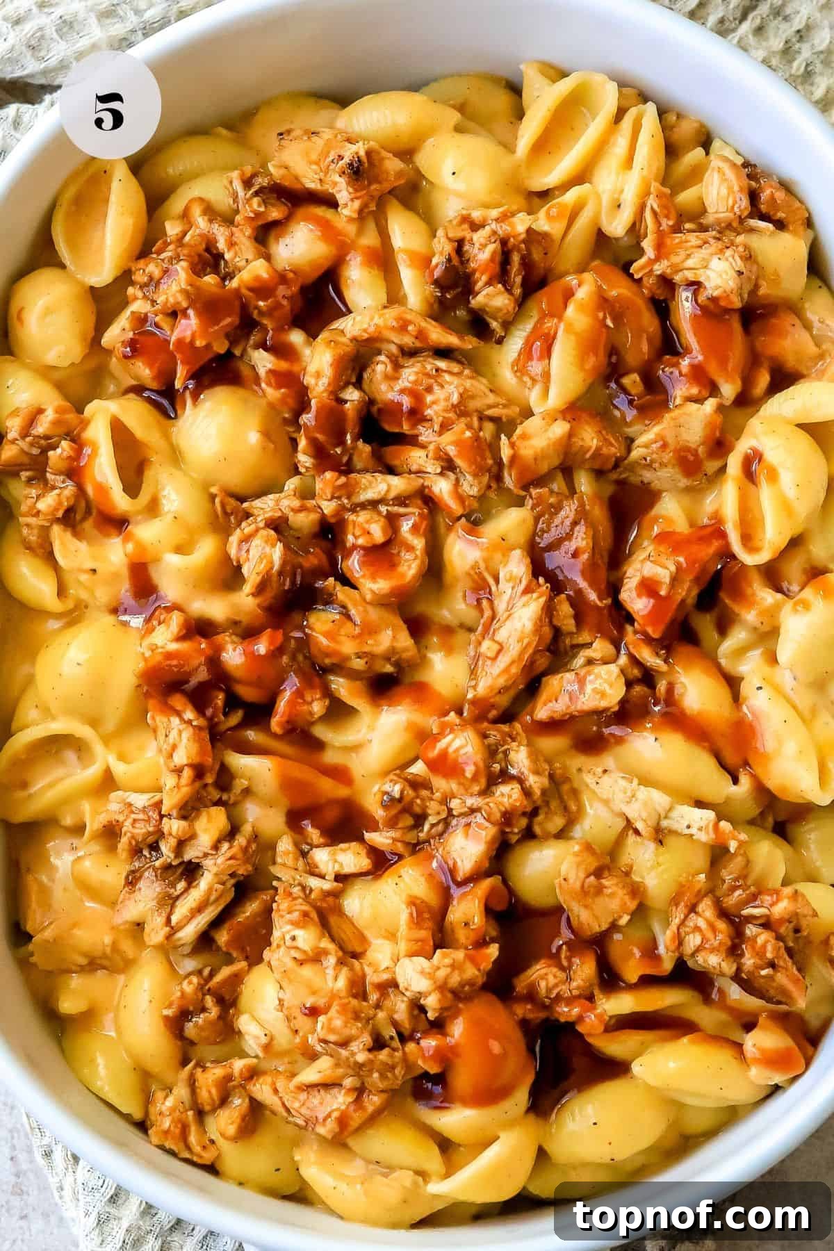 SMOKED BBQ CHICKEN MACARONI AND CHEESE 5 A baked white casserole dish generously filled with golden-brown cheese shells and BBQ chicken, fresh from the oven.