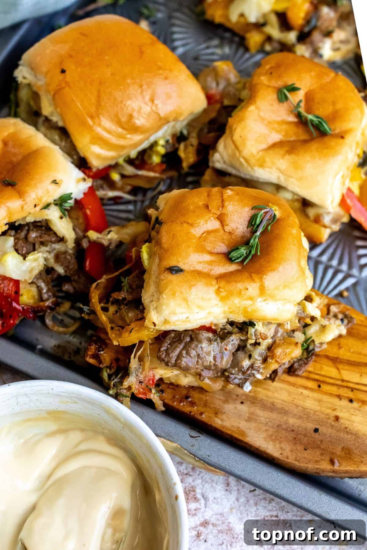 An overhead image of philly cheesesteak sliders on a serving plate.