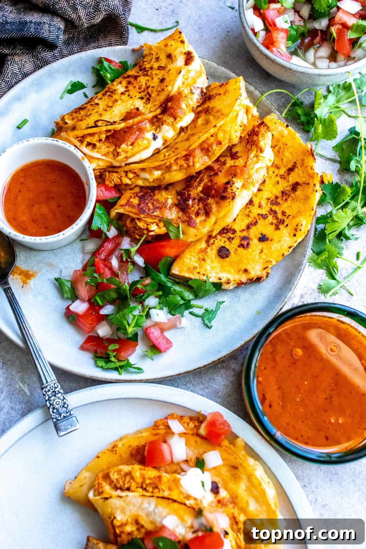Mouthwatering Chicken Birria Tacos 2 Two Chicken Birria Tacos on a grey plate, drizzled with rich red sauce, garnished with fresh pico de gallo and cilantro, with extra dipping consomé on the side.