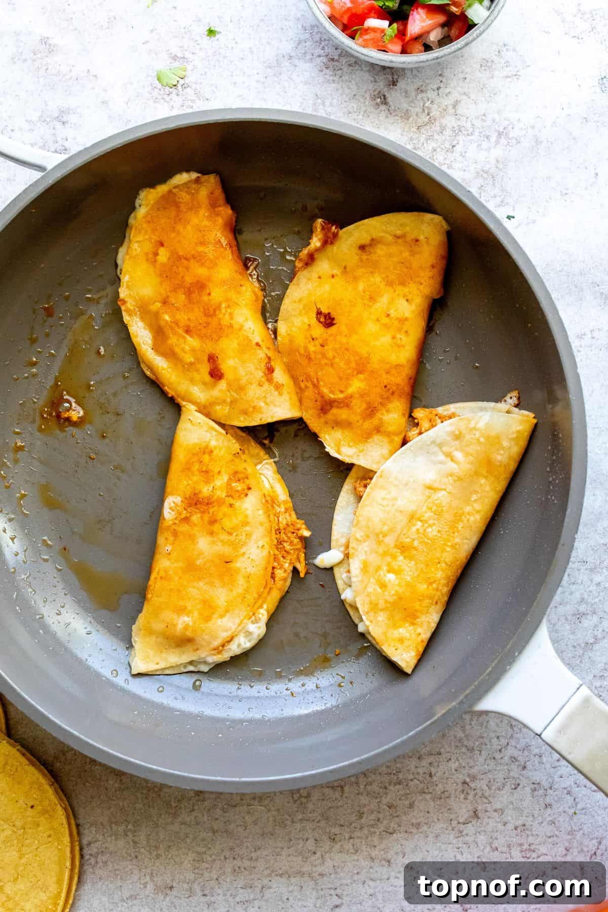 Mouthwatering Chicken Birria Tacos 5 Hands assembling Chicken Birria Tacos on a hot skillet, with a tortilla brushed with sauce, shredded cheese, and birria chicken filling.