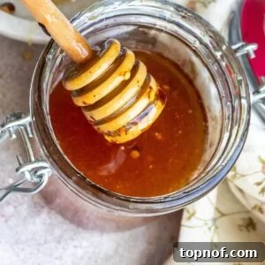 A jar full of honey with a honey stick.
