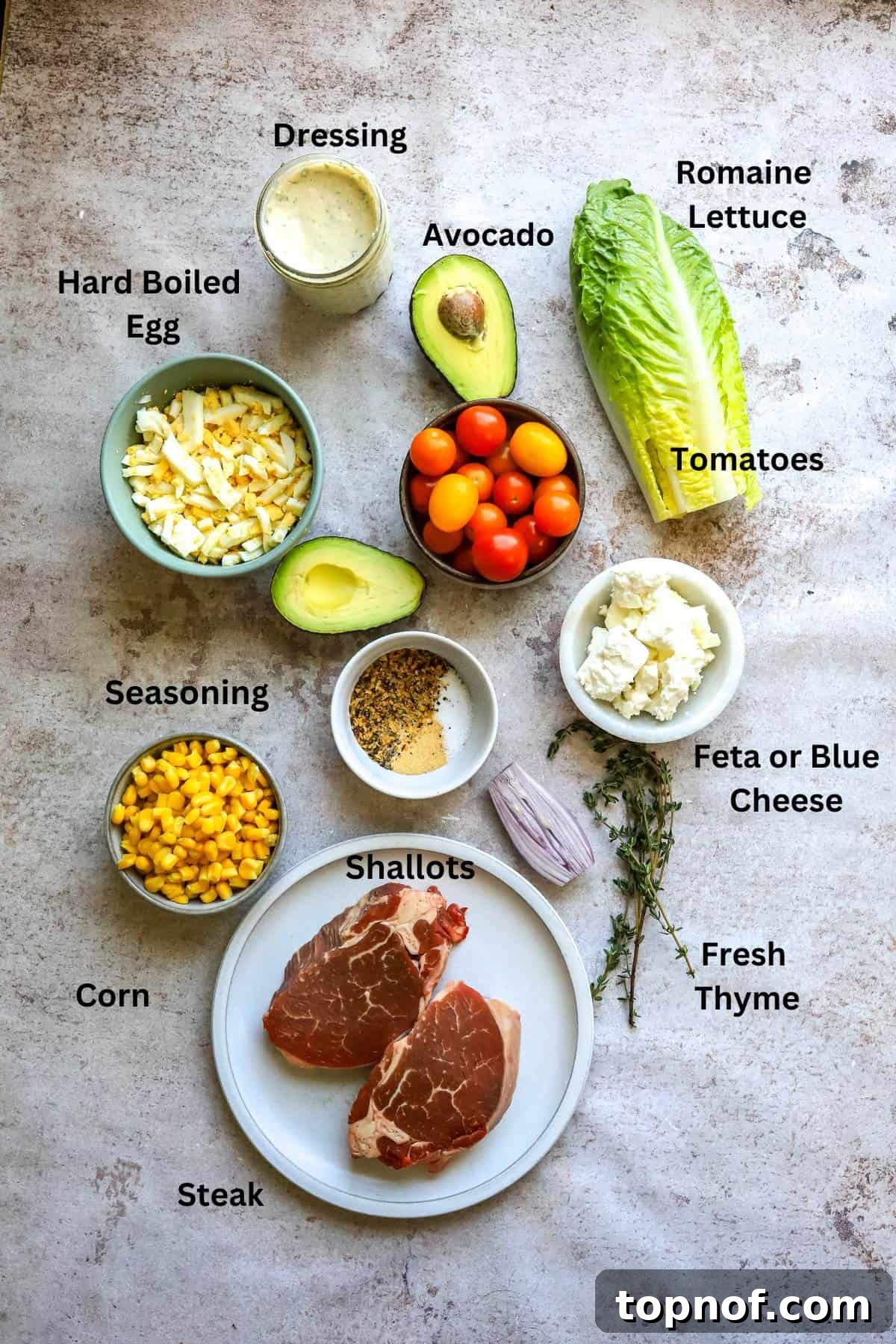 Hearty Steak Salad 3 A collection of fresh ingredients for steak salad, including lettuce, tomatoes, corn, and avocado, arranged on a kitchen counter.